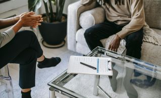 Crop anonymous African American man in casual clothes sitting on sofa and talking to female psychologist during psychotherapy session in modern studio